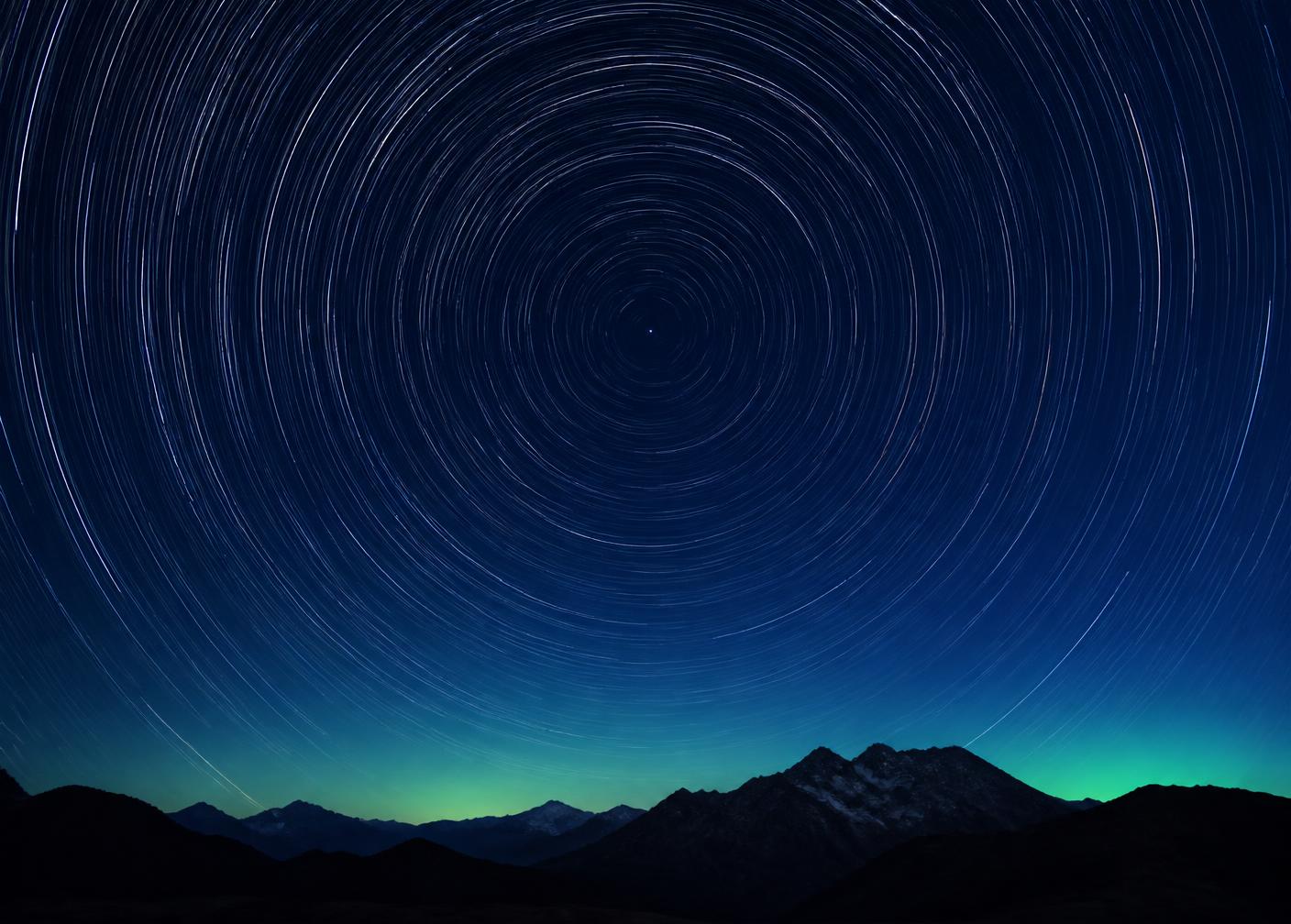 Long exposure night sky photograph with star trails arcing above a dark horizon